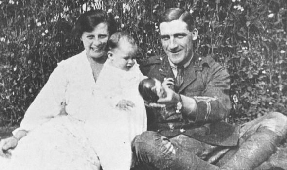 A photograph of Bessie, sat next to Charlie in his uniform. Their daughter, the infant Pauline, sits on their laps. Charlie holds a toy and gestures towards the camera to encourage her to look in its direction.
