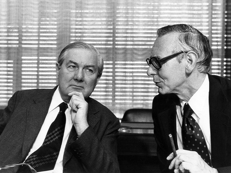 This is an image of James Callaghan, British Secretary of State for Foreign and Commonwealth Affairs, on the left, and Max van der Stoel, Dutch Minister for Foreign Affairs, on the right. The men are both dressed in suits and are engaging in conversation. Photo taken 1975.