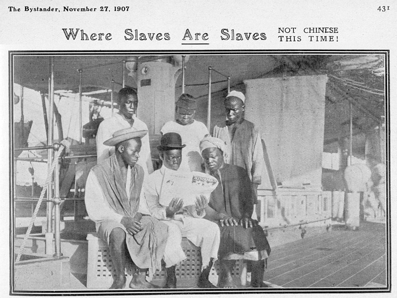 Black and white photograph from The Bystander, dated 27 November 1927, titled Where Slaves Are Slaves, Not Chinese This Time!, showing 6 African men reading a copy of The Bystander.