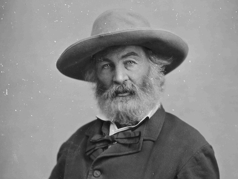 A photograph of Walt Whitman. It is in black and white, he has a large hat and beard.