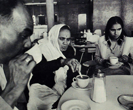 A photograph of an immigrant family sat around a table enjoying a cup of tea together.