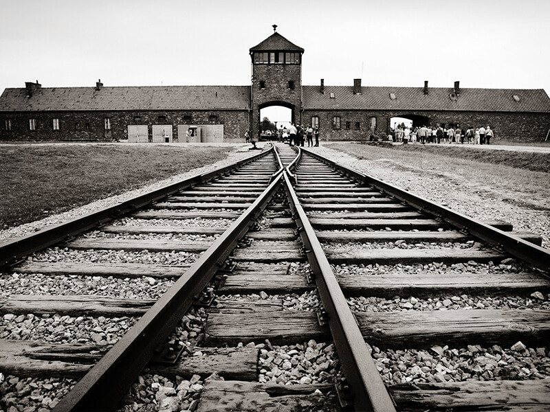 A photograph of the entrance to Auschwitz-Birkenau with train track running towards the camp in the foreground.