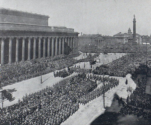 A black and white photograph of a parade of 12,000 soldiers in Liverpool. The photograph shows part of the forty-five minute parade passing by Liverpool’s St. George’s Hall, which had been a recruitment headquarters in the city centre since the war’s outbreak.