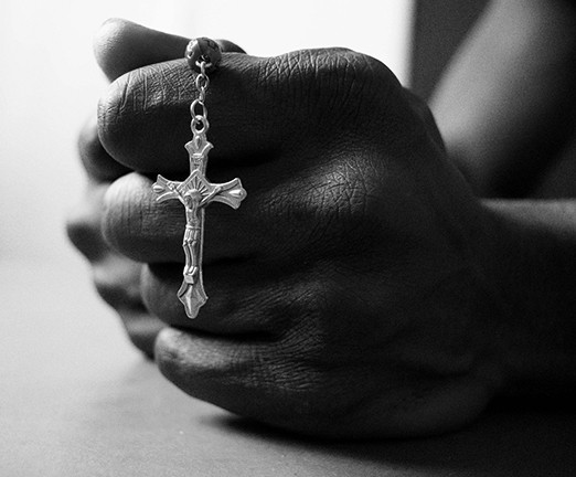 A pair of hands clasped together, clutching a necklace with a cross pendant.