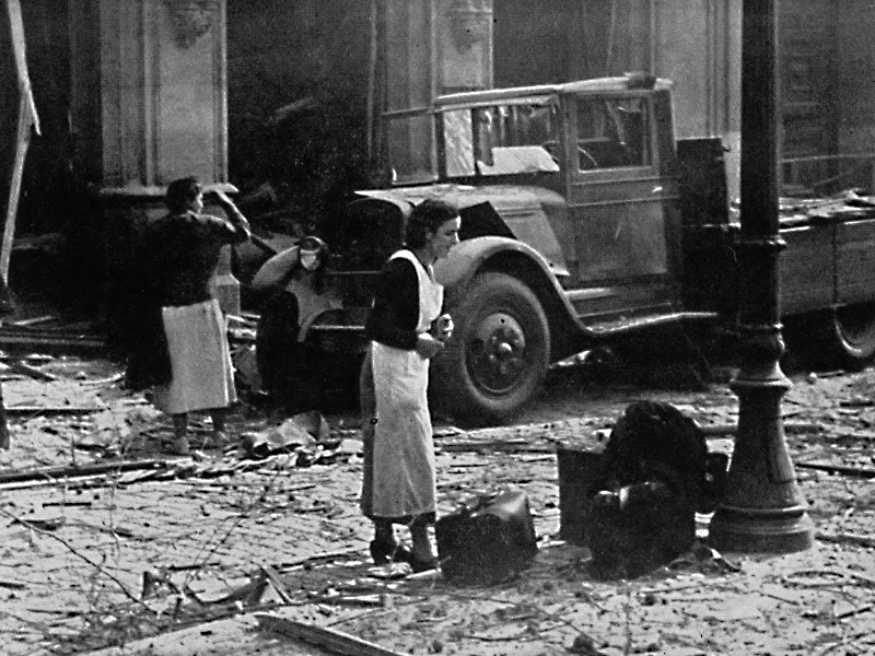 Black and white photograph of a nurse in a street covered in rubble.