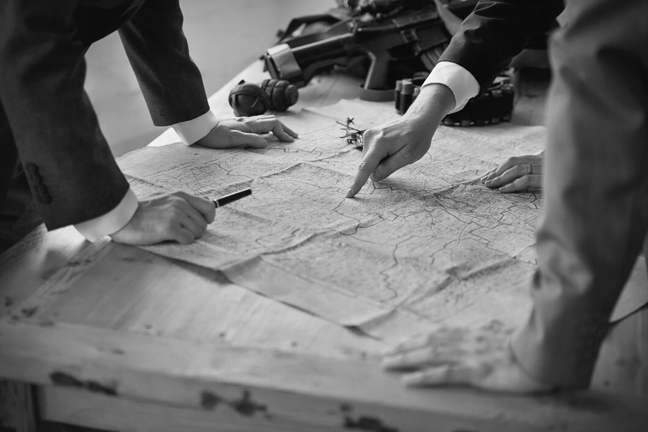 A map laid across a table. People are stood around the map and pointing at areas.