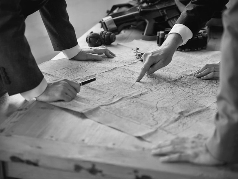 A map laid across a table. People are stood around the map and pointing at areas.