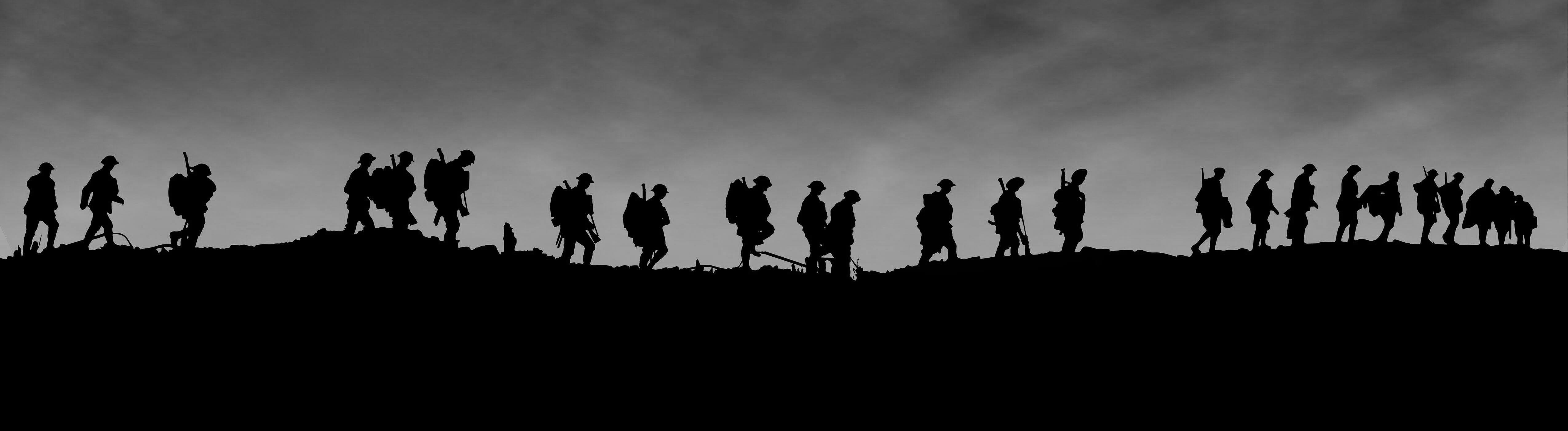 A silhouette image of soldiers walking across a hill, carrying their equipment.