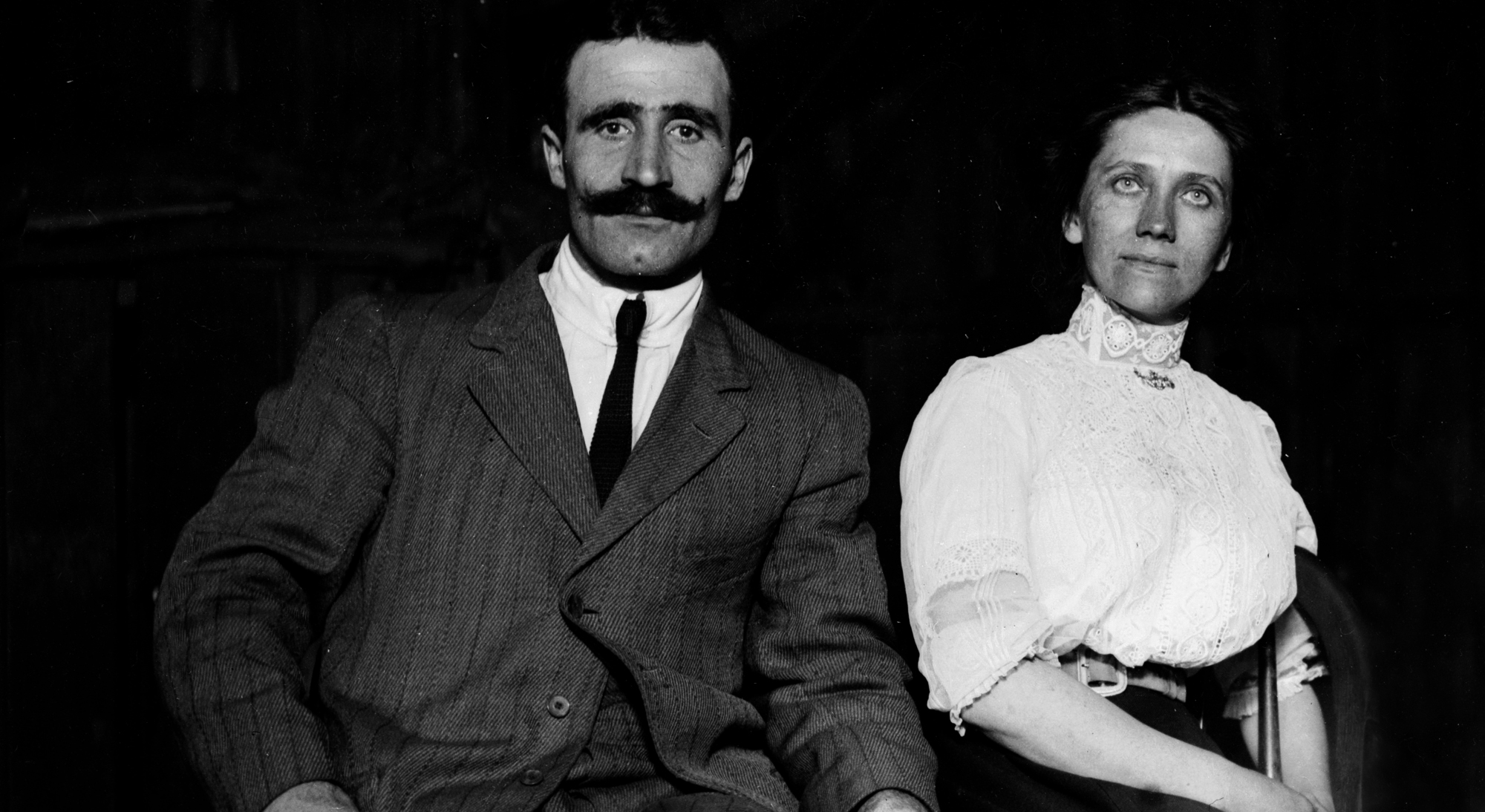 On the left, a man wearing a suit, and on the right, a woman wearing a white blouse.