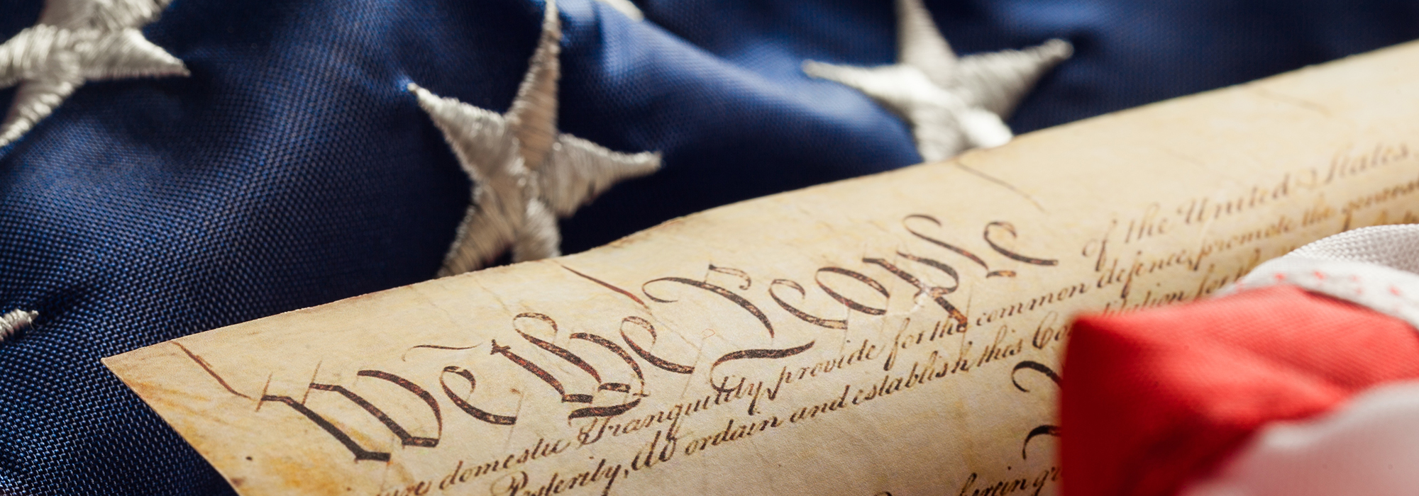 An image of the US constitution laid on top of a USA flag. On top of the constitution in big letters it says 'We the People'.