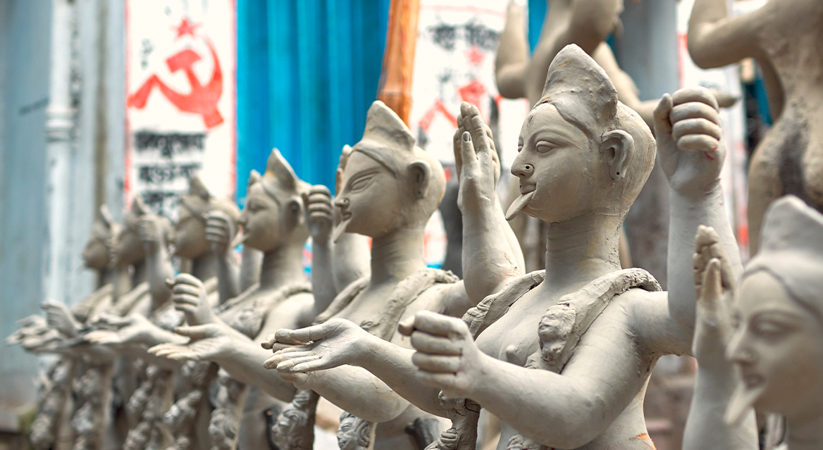 Clay idols of Hindu Goddess Kali. A communist party election campaign graffiti is seen on a building wall behind.