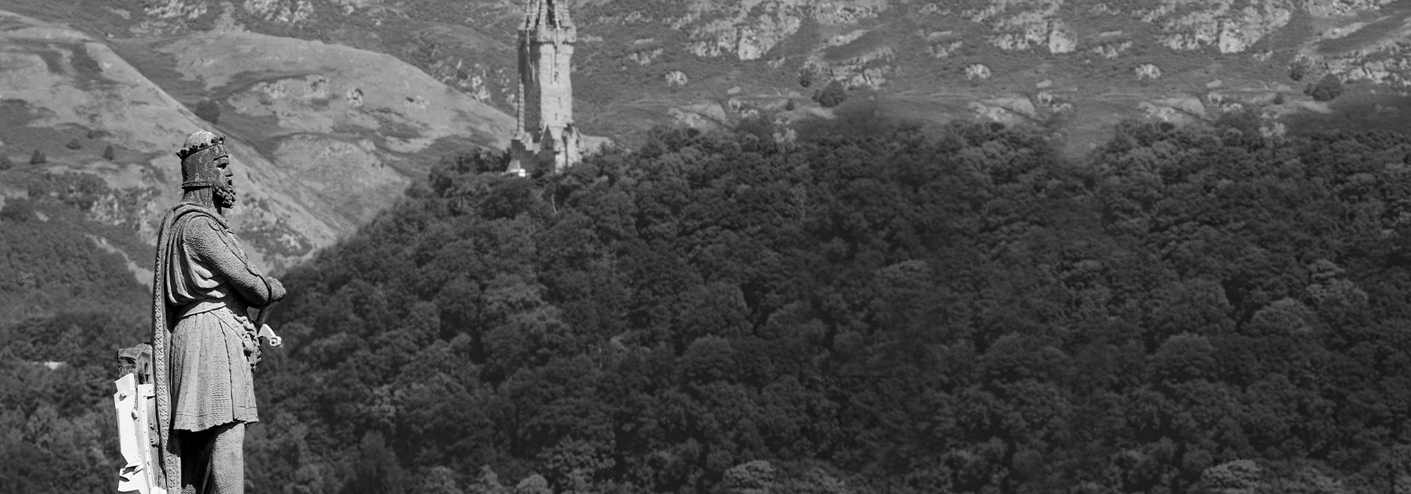 A black and white photo of the Statue of Robert the Bruce at Stirling Castle and the Wallace Monument is seen in the distance.