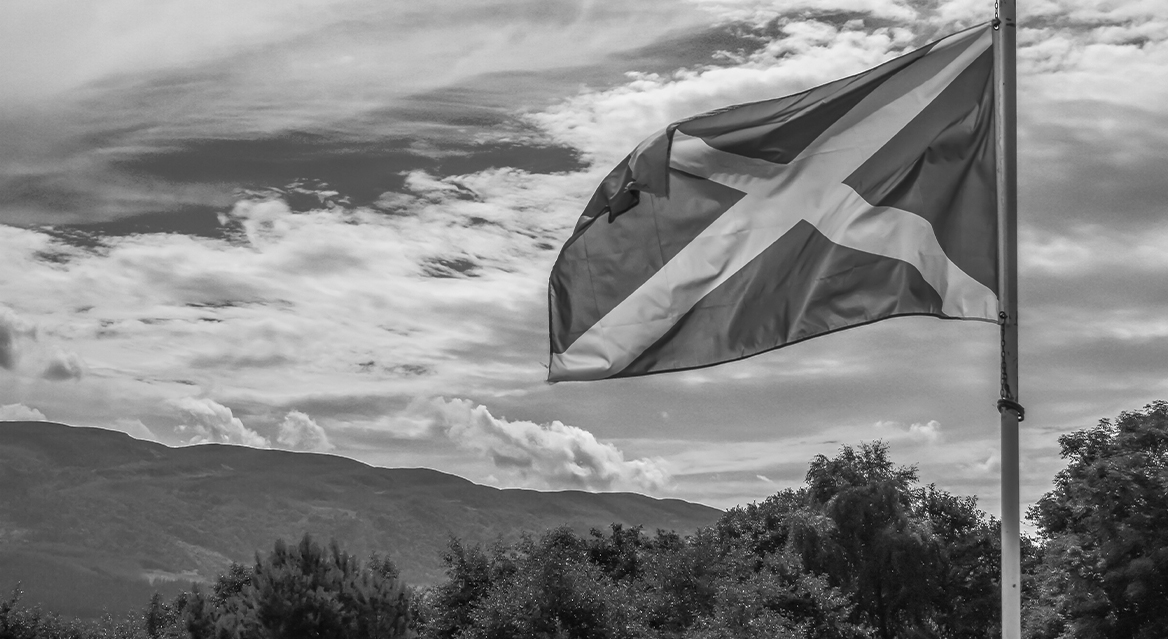 A black and white image of a Scotland flag in the wind in the countryside.