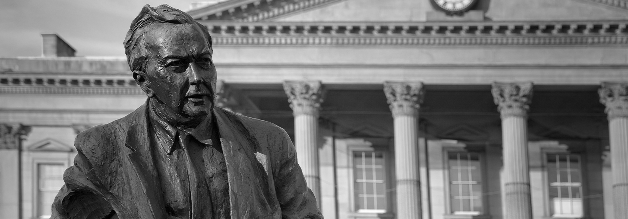 This image shows the head and shoulders of a statue of Harold Wilson in the foreground, with Huddersfield train station in the background.