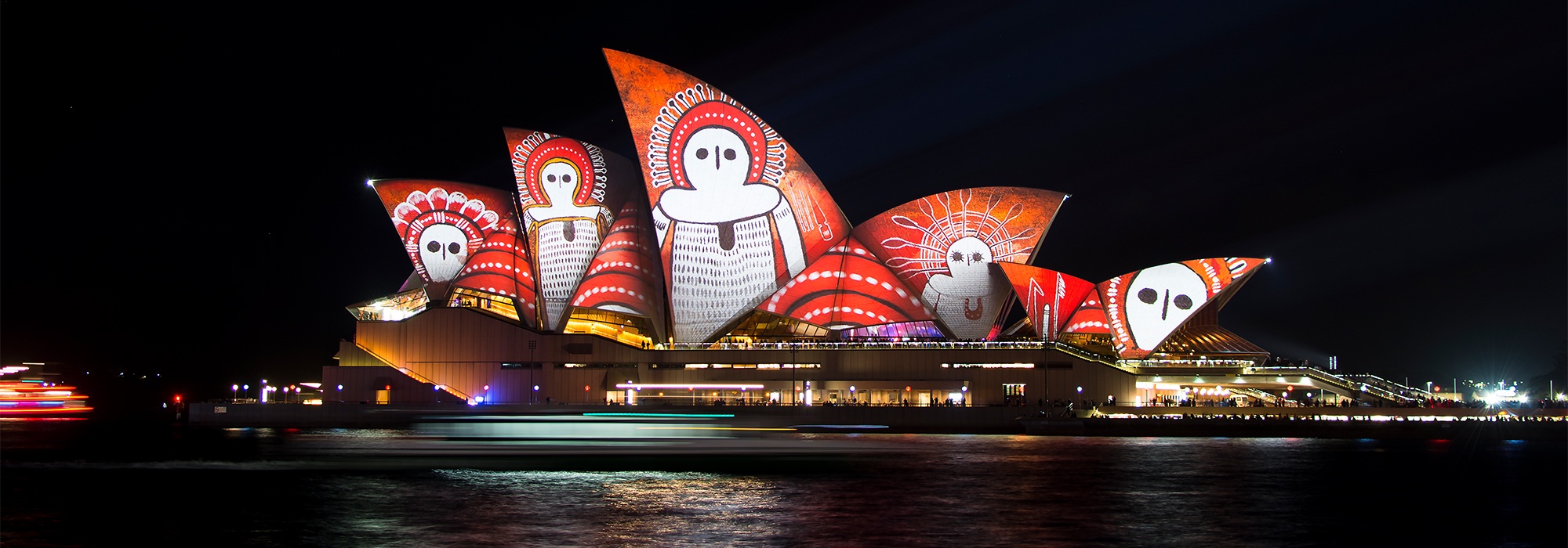 A photograph of Sydney Opera House illuminated in lights for 'Vivid Sydney' a light festival with abstract designs, vivid colours and aboriginal artwork.