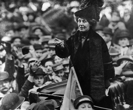 A photograph of Emmeline Pankhurst in an old car whilst people crowd around the car.
