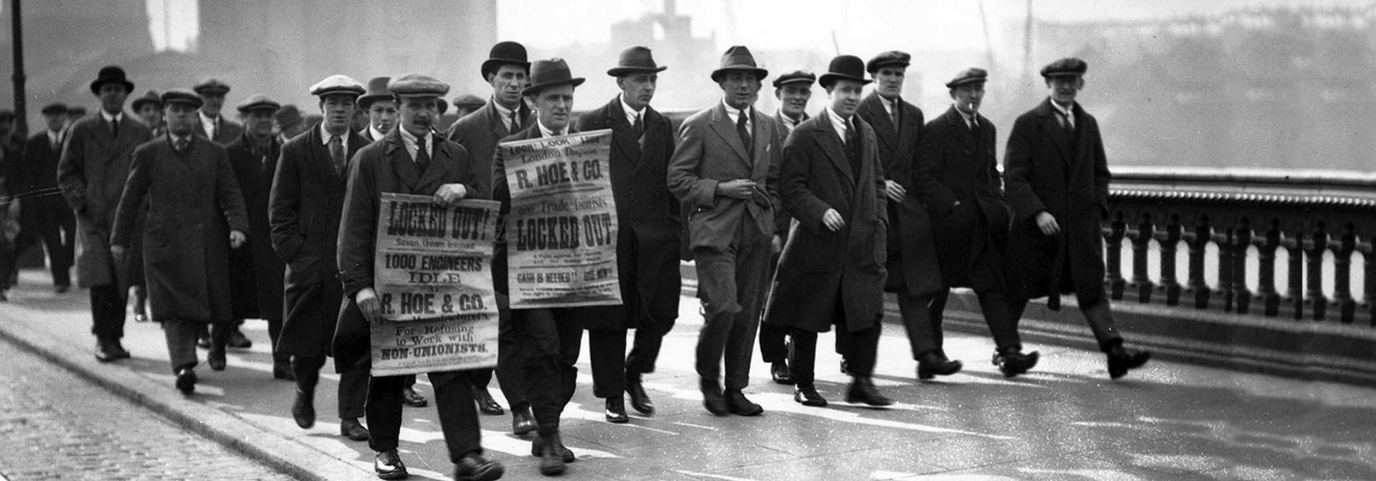 A black and white image of workers on strike, holding up posters and marching.