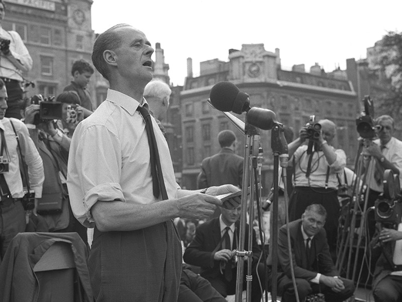A black and white image of John Gollan giving a speech into microphones.