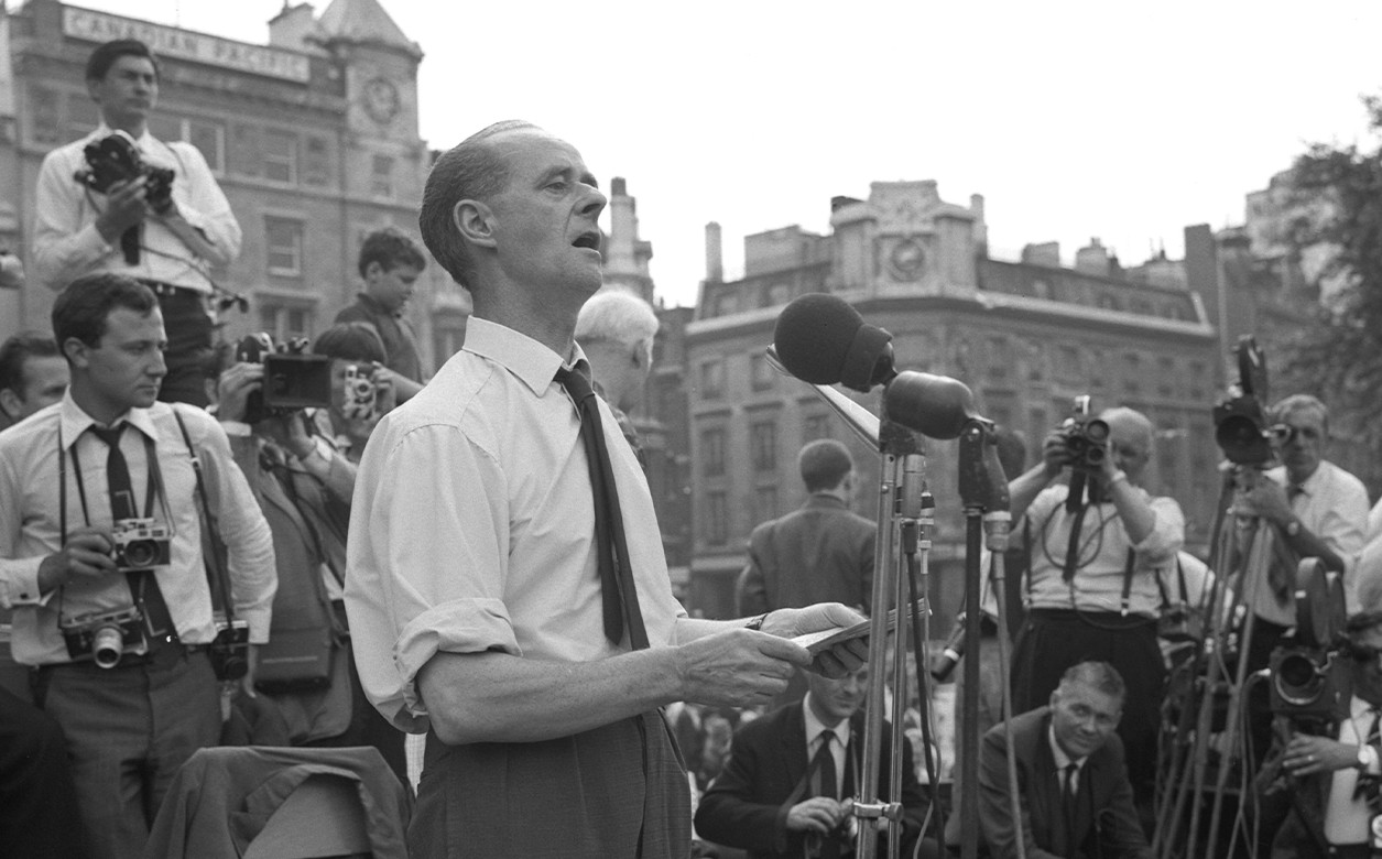 A black and white image of John Gollan giving a speech into microphones.