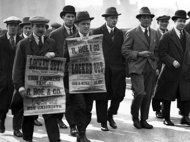 A black and white image of workers on strike, holding up posters and marching.