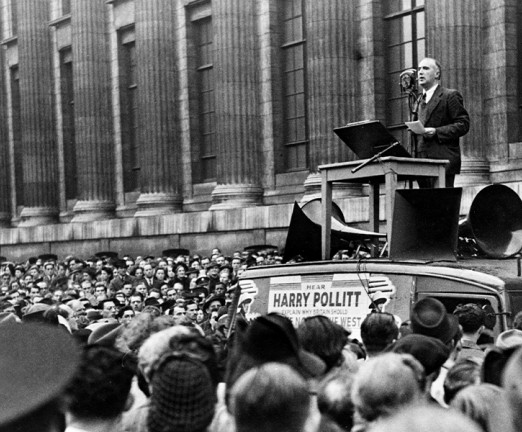 A black and white photograph of Harry Pollitt, General Secretary of the British Communist Party, speaking to large crowds gathered below a podium.