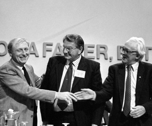 Retiring Labour leader Michael Foot shakes hands with new leader Neil Kinnock (left) watched by Eric Heffer, in Brighton, at the Labour Party Conference.