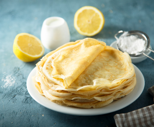 A photograph of a stack of pancakes with lemons and sugar beside it.