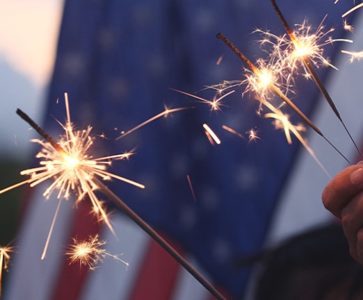 Three sparklers are lit against the background of the USA flag.