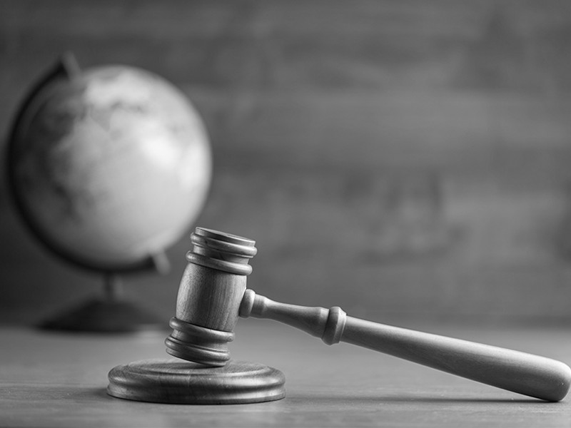 A black and white image of a gavel resting on a table with a globe in the background.
