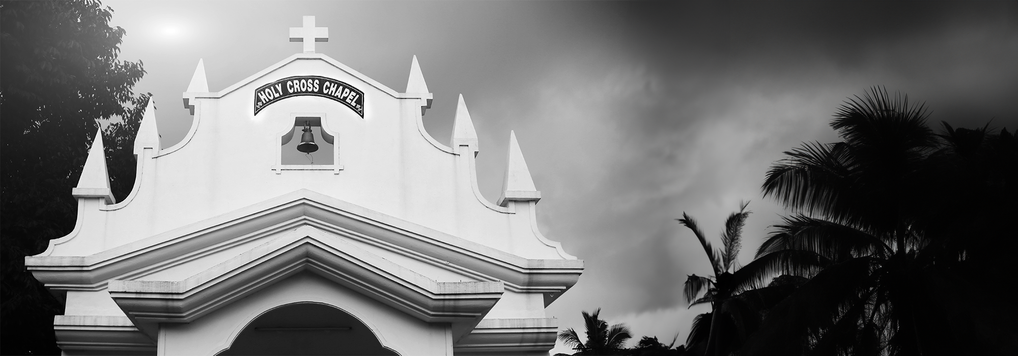 A black and white photograph of a church in Goa, with a sign that reads "Holy Cross Chapel".