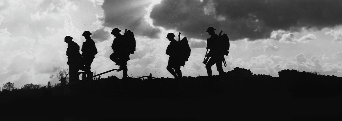 A black and white silhouette image of soldiers walking and carrying their equipment. The soldiers are walking from right to left.