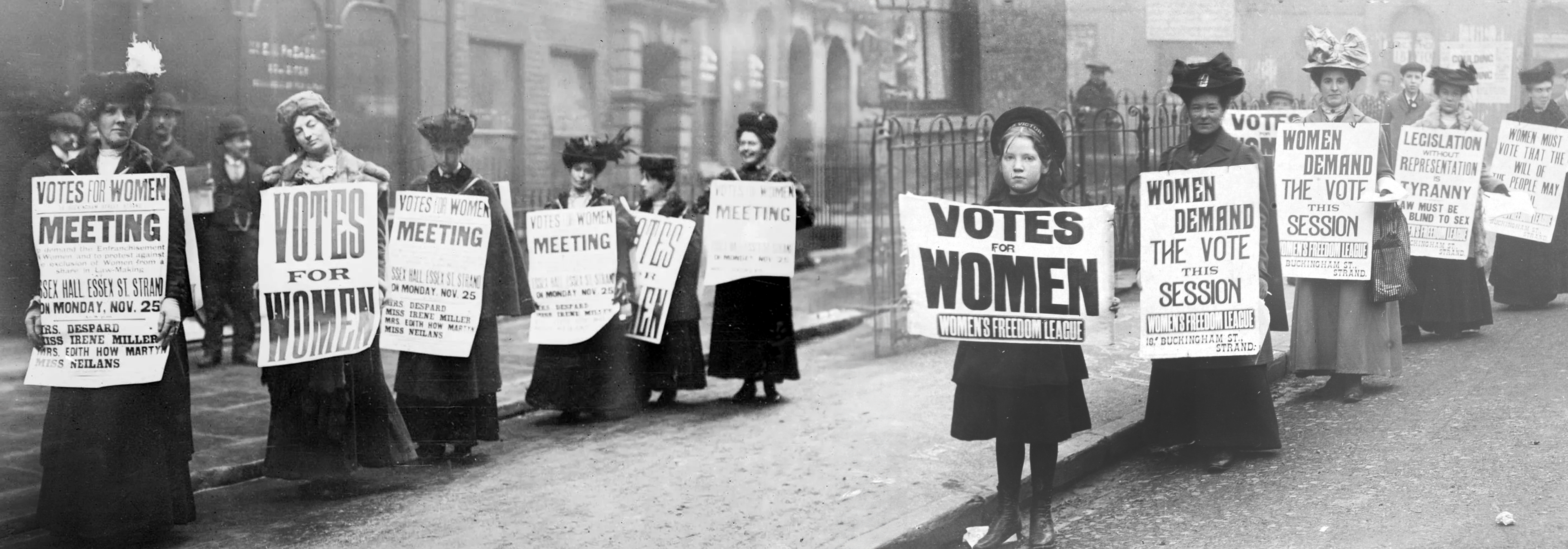 1907 photgraph showing women from the Women's Freedom League holding posters that state "Women Demand The Vote" and "Votes For Women".