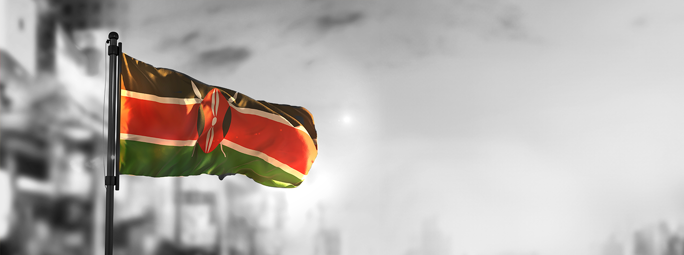 Kenyan flag against a blurred city background at sunrise.