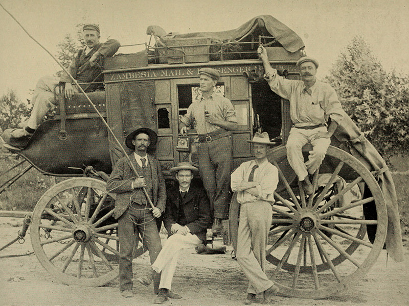 Six men stood and sat around a wagon - the first run of the Zambesia Mail and Passenger Company stage coach between Salisbury (now Harare) and Umtali (now Mutare), Southern Rhodesia (now Zimbabwe).