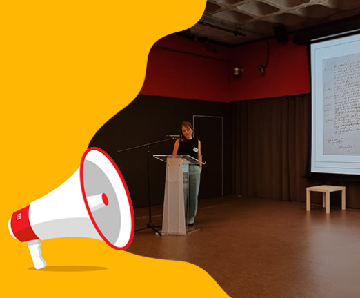 Mary Wills, a woman wearing a black top, stands at a desk while she presents on a screen behind her. There is an overlayed illustration of a megaphone.