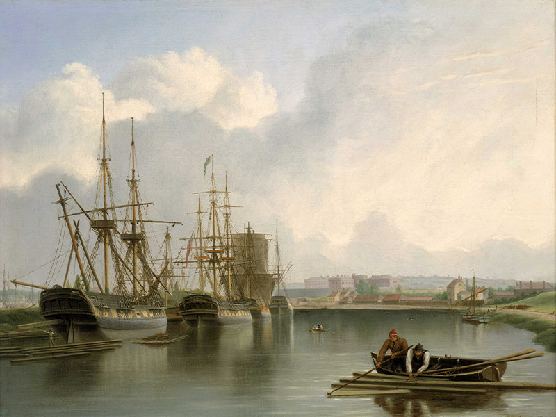 A painting showing West Indiamen alongside Bristol docks on the Avon. The ship in the foreground on the left is being unloaded with timber from America. Some of the unloaded timber floats on the water. A man can be seen standing on a pile of floating planks as one of them is being lowered down from the ship. A figure leans over the stern to manage the process. The ship may be having her mast stepped. There is another pile of wooden planks floating on the starboard side of the ship. Two men in a rowing boat are using a pole and hook to catch a smaller pile of planks floating in the foreground on the right. The barge on the right is a Severn trow which conveyed a lot of cargo up and down the river, and, as in this painting, would have brought iron down the Severn.