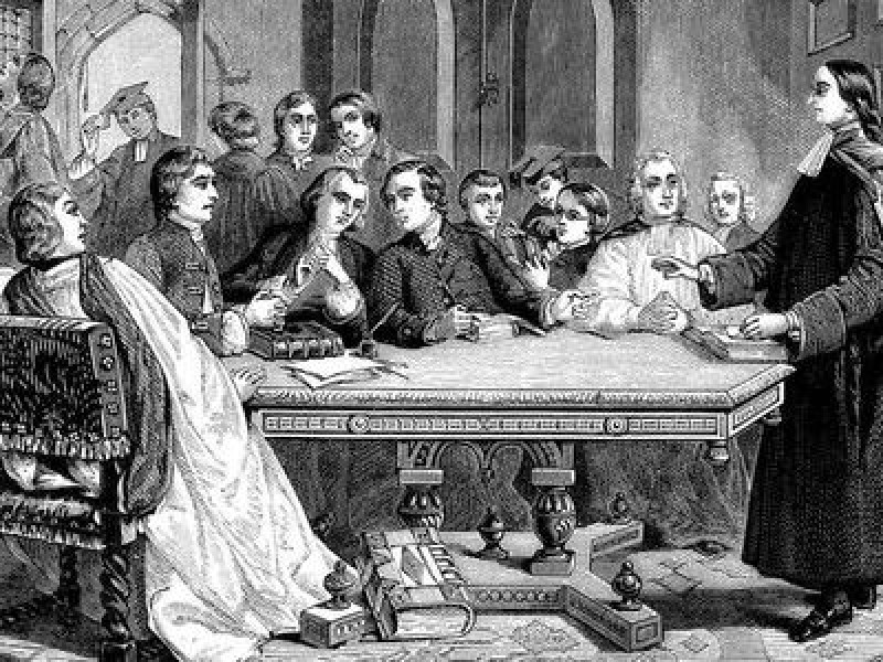 John Wesley stands at the head of the table, with a crowd of men sat around it. This illustration depicts the beginnings of the Methodist church