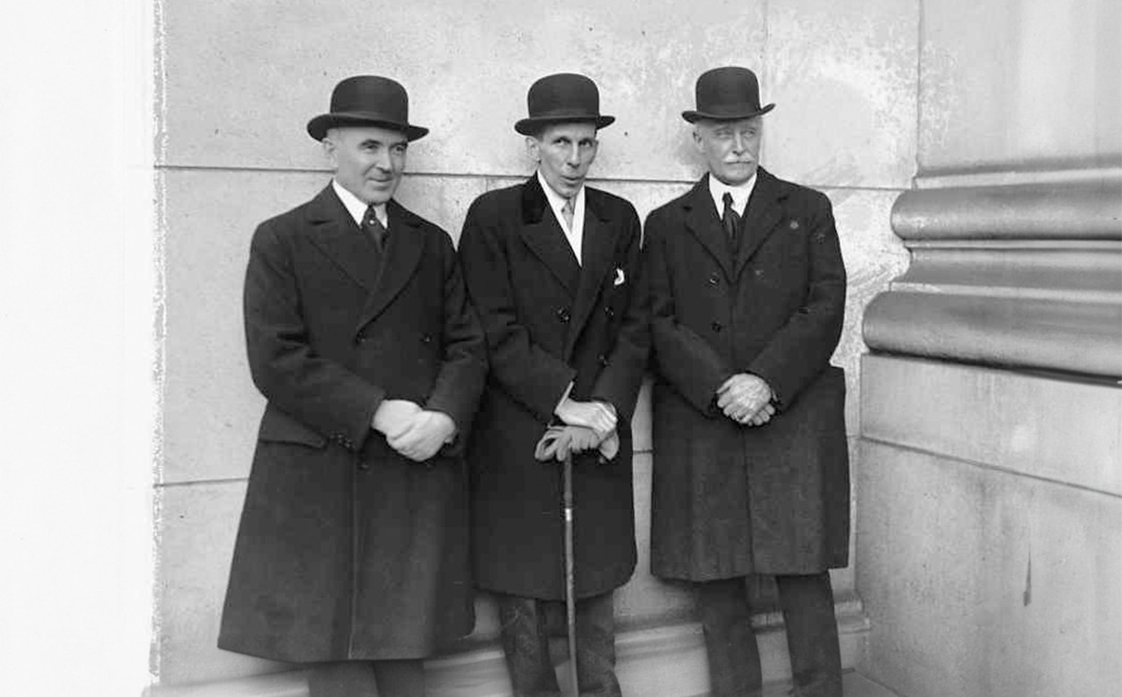 Smiddy, Massey, and Howard, in hats, stood against a stone wall