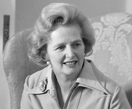 A black and white photograph of Margaret Thatcher in 1975, a woman wearing a collared blazer, with short hair. She looks off in to the distance.
