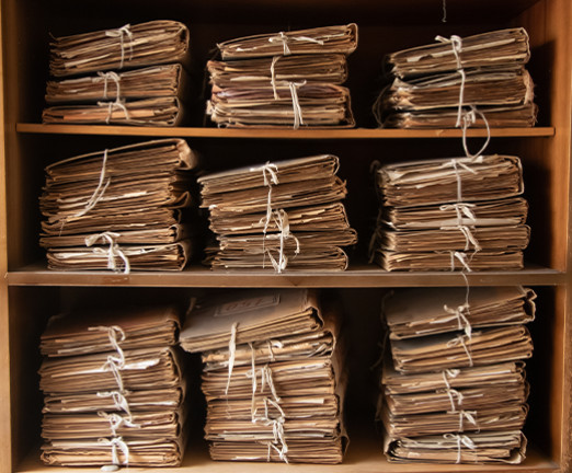 A shelving unit with piles of archival documents stacked neatly, tied with a white ribbon and placed in rows on the shelves.